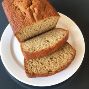 "Freshly baked banana bread on a cooling rack, surrounded by a cup of tea, bananas, and a jar of sugar, showcasing a traditional UK-style recipe."